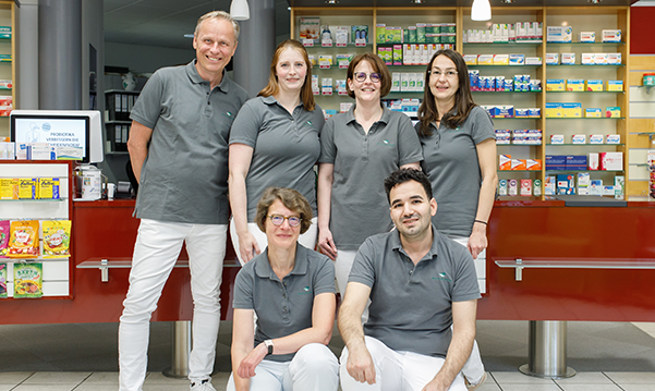 Team und Inhaber der Trierweiler Apotheke in Trierweiler stehen in der Apotheke für ein Gruppenfoto zusammen.